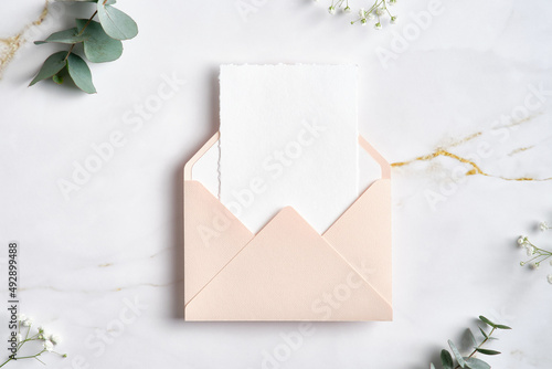 Pink envelope with white paper card inside and eucalyptus branches on marble table