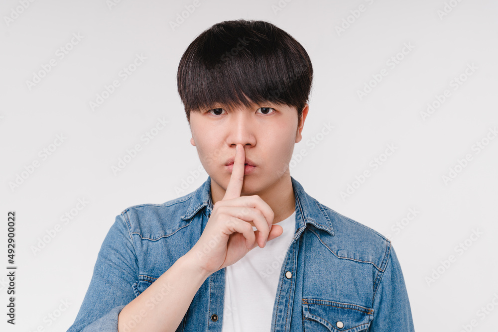 Cropped closeup portrait of handsome young asian korean man showing silent gesture, finger in lips isolated in white background. Secret concept Cropped closeup portrait of handsome young asian korean man showing silent gesture, finger in lips isolated in white background. Secret concept