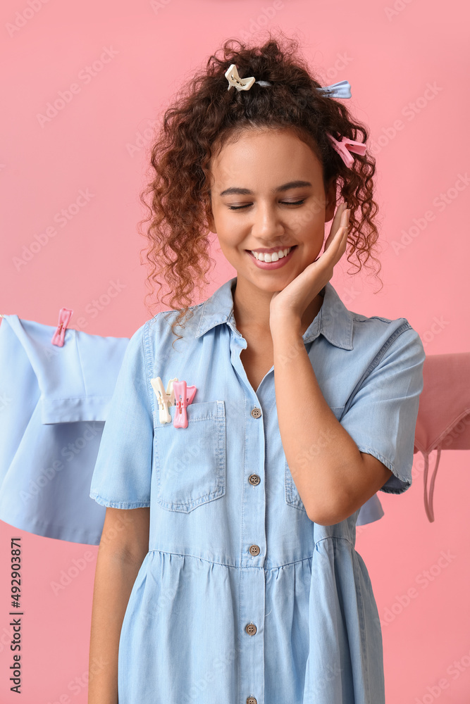 Young African-American woman with hanging laundry and plastic clothespins on pink background Young African-American woman with hanging laundry and plastic clothespins on pink background