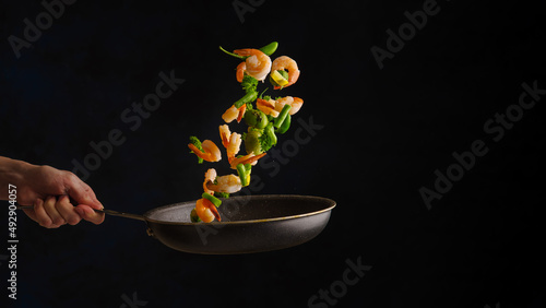 Chef roasts shrimp with vegetables on black background .freezing in motion.Seafood food.Concept of cooking and gastronomy. Black background for text