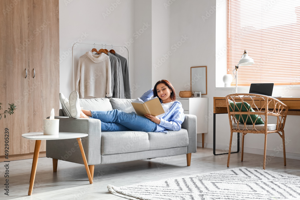 Beautiful woman with book resting on couch at home Beautiful woman with book resting on couch at home