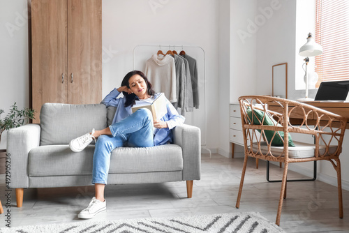 Beautiful woman with book resting on couch at home