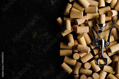 Metal corkscrew for opening wine corks against background of wine corks.On black background with space for text, top view.Concept of wine sales and advertising. Banner photo
