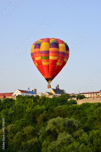 A multi-colored inflatable balloon with a gondola flies over the ancient city and the green forest