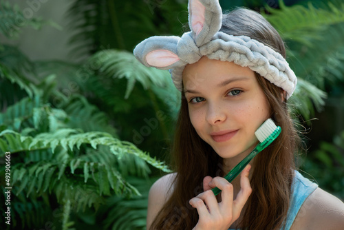Portrait of beautiful little girl with funny bunny headband is using cleansing facial brush and face mousse cream for skincare.  Pretty kid cleansing and moisturize her skin