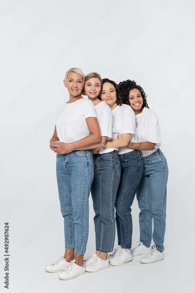 Full length of smiling multiethnic women embracing on grey background, feminism concept. Full length of smiling multiethnic women embracing on grey background, feminism concept.