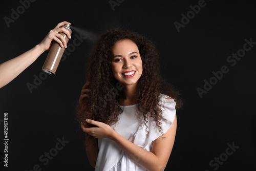 Beautiful young African-American woman and hand with hair spray on black background © Pixel-Shot