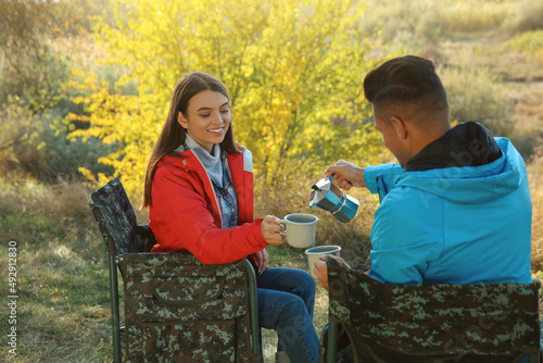 Couple resting in camping chairs and enjoying hot drink outdoors