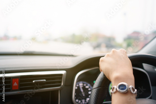 Unrecognizable female driver using left hand grabs on the steering wheel while driving on the road.