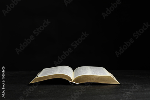 Open Bible on black table against dark background. Christian religious book