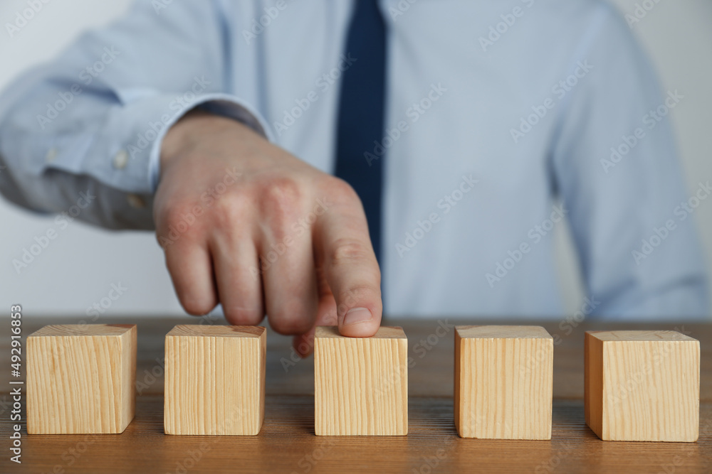 Businessman arranging blank cubes on wooden table, closeup. Space for text Businessman arranging blank cubes on wooden table, closeup. Space for text