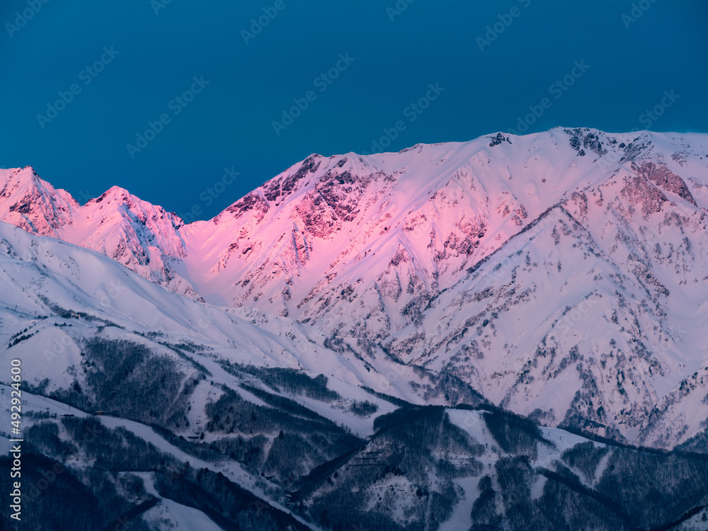 冬の北アルプス、夜明けの太陽の光りが雲に遮られ、山肌がスポットライト状に照らし出されてピンク色に染まる、モルゲンロート。