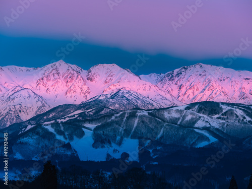 冬の北アルプス、夜明けの太陽の光りが雲に遮られ、山並みが直線状に照らし出されてピンク色に染まる、モルゲンロート