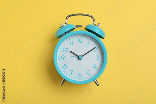 Alarm clock on yellow background, top view. School time