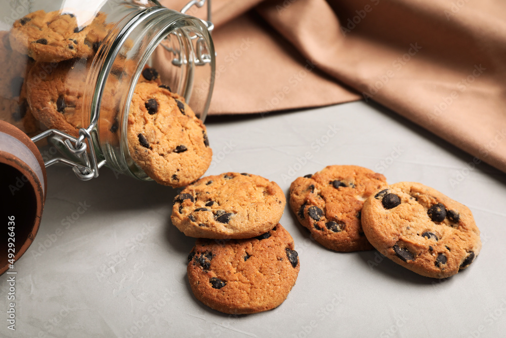 Overturned glass jar with delicious chocolate chip cookies on light grey table, closeup Overturned glass jar with delicious chocolate chip cookies on light grey table, closeup