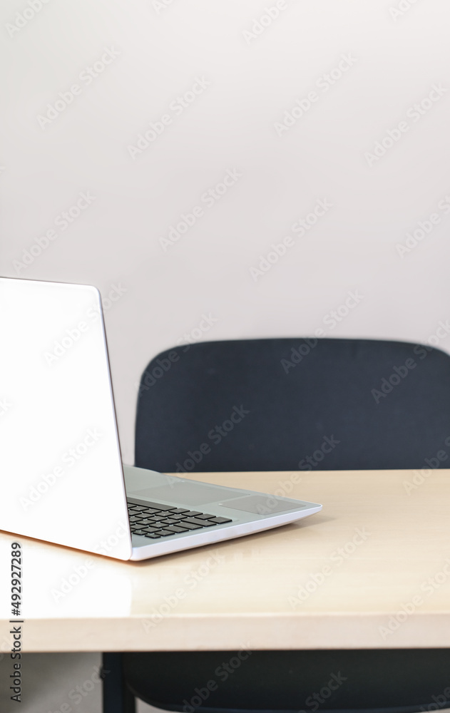 Fototapeta premium empty workplace with laptop on a wooden desk. black office chair. copy space. vertical size.