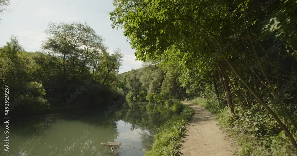 POV shot, walking along a quiet river with green trees and bushes around it. Iskar-Panega eco trail, Bulgaria. POV shot, walking along a quiet river with green trees and bushes around it. Iskar-Panega eco trail, Bulgaria.