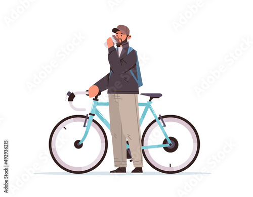 male cyclist taking break during bike ride man with takeaway coffee cup standing near bicycle