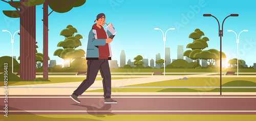 man drinking coffee with straw and using smartphone while walking in urban park social media communication