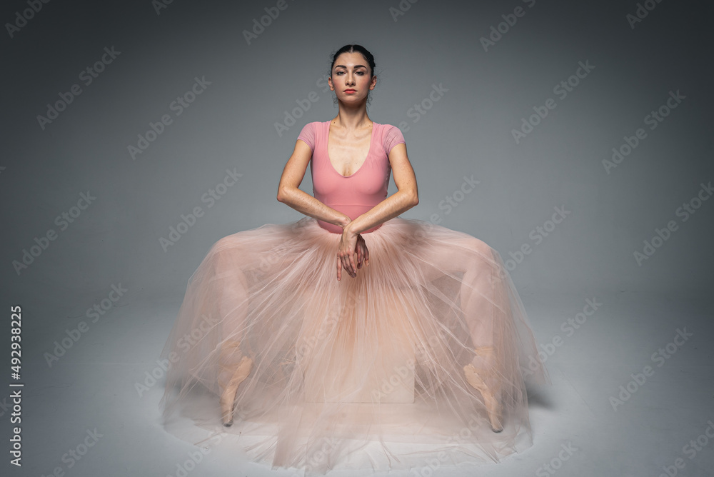 Naklejka premium young pretty, fragile, beautiful ballerina dancing in a long pale pink dress with tulle on a uniform background, hand movements, restrained tone. Ballet, dance, dancer. Place for inscription
