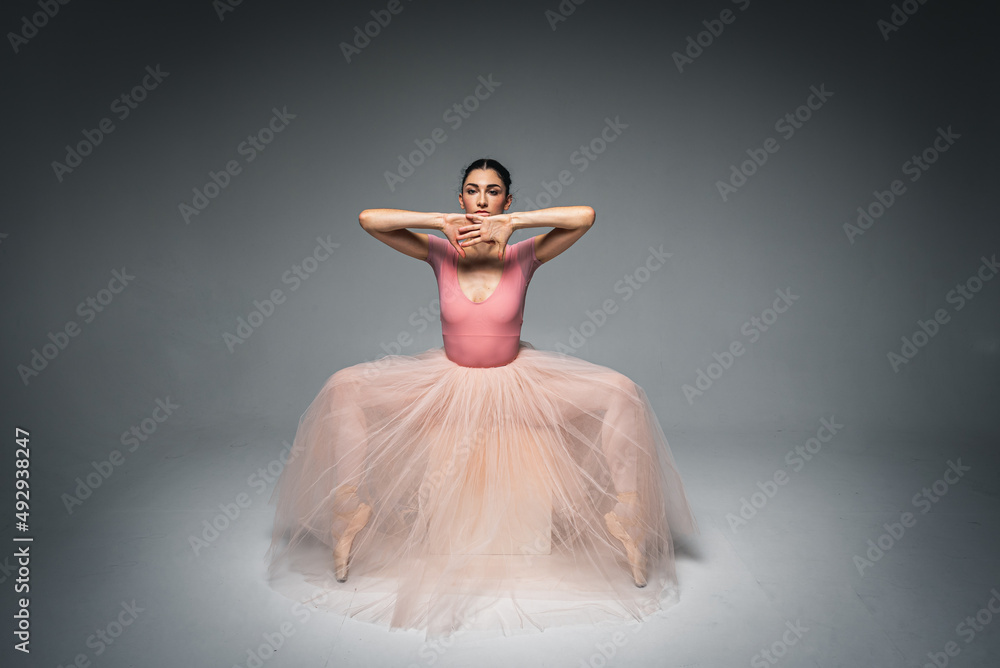 Fototapeta premium young pretty, fragile, beautiful ballerina dancing in a long pale pink dress with tulle on a uniform background, hand movements, restrained tone. Ballet, dance, dancer. Place for inscription