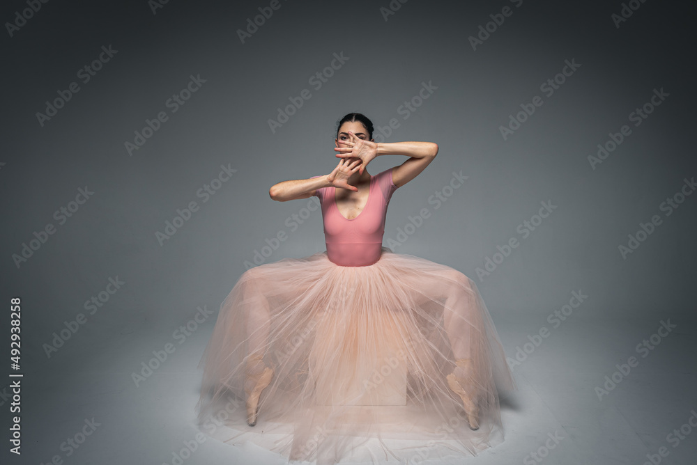 Naklejka premium young pretty, fragile, beautiful ballerina dancing in a long pale pink dress with tulle on a uniform background, hand movements, restrained tone. Ballet, dance, dancer. Place for inscription