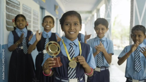 Proud girl with winner trophy and medal with cheeful students applauding for success of kid - concpet of inspiration, encouragement and intelligence photo