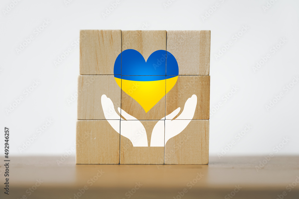 heart with print the national flag of Ukraine on wooden cube block above white hand icon heart with print the national flag of Ukraine on wooden cube block above white hand icon