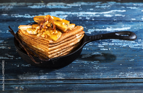 Pancakes caramelized with bananas, honey and nuts in a cast-iron frying pan. Thin pancakes or crepes