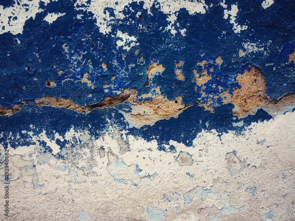 surface of the old cement wall, painted white and blue, has cracks.