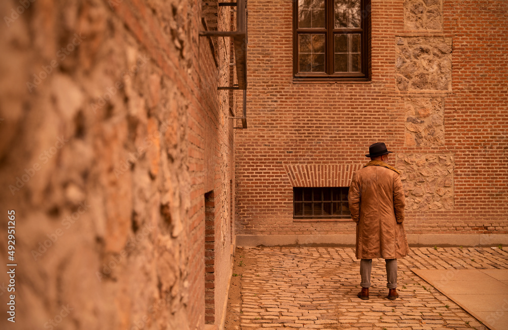 Fototapeta premium Rear view of man in coat standing in front of old building on street during sand storm day. Madrid, Spain