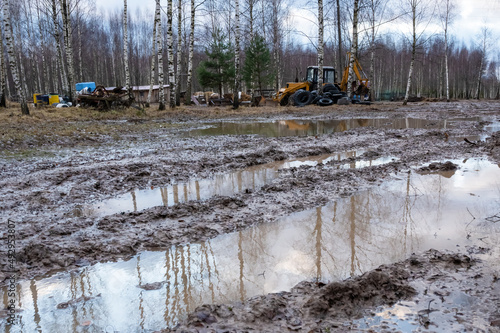 Rural muddy dirt road late autumn after rain. Off-road, wild dirt trail with large puddles background agricultural machinery, tractors, showing difficulties of movement rural areas during rainy season