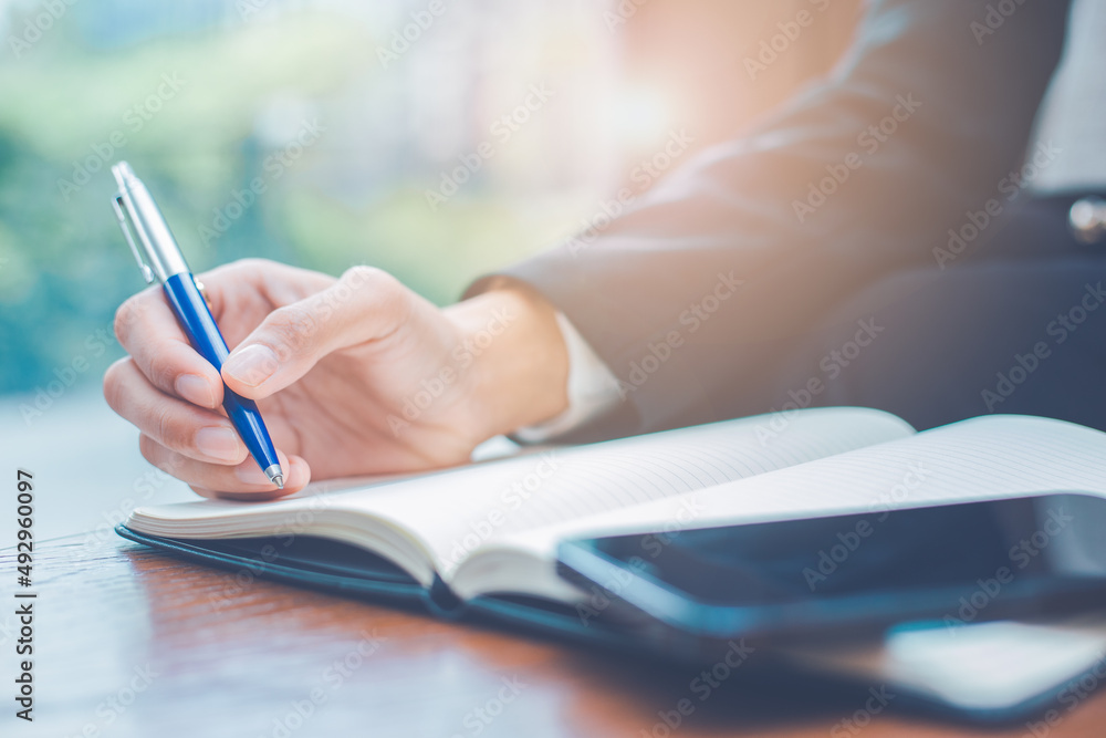 Woman hand writing on a notepad with a pen in the office.There is a mobile phone on the table.