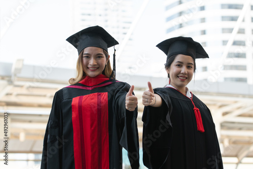 Happy Asian young beautiful graduate students with master and bachelor University degree with black board cap with red tassels is smiling and thumbs up. Concept of graduation ceremony