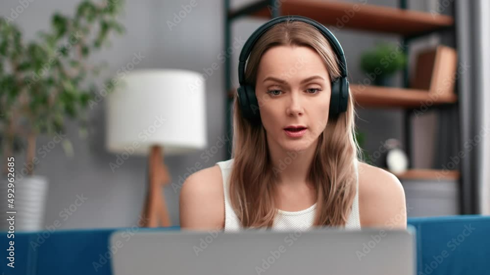 Modern woman in headphones talking online video call consulting remotely use laptop at home Modern woman in headphones talking online video call consulting remotely use laptop at home