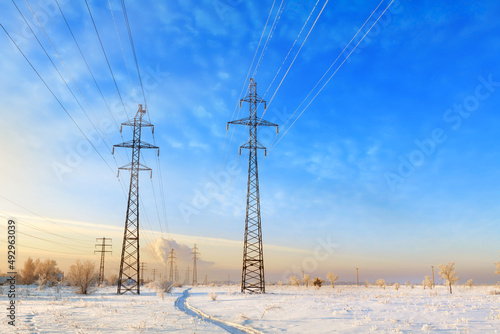 High voltage power lines at sunset. Winter landscape. Metal poles with high electrical load against the blue sky.