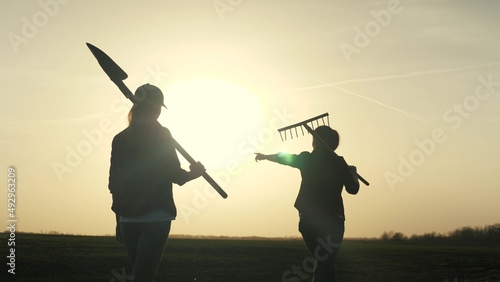 Farmer girls walk across the field to work with a shovel and rake at sunset in the sky, young and adult women are going to grab the earth, business on growing plants in the countryside outdoors, life