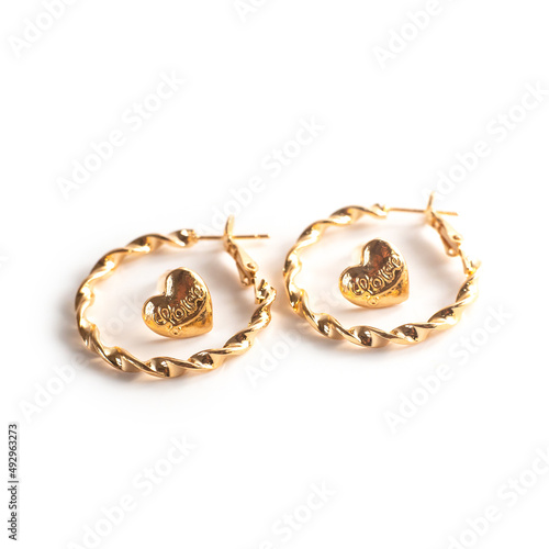 Set of two pairs of earrings. Close up gold metal jewelry heart stud earrings "Love" and gold hoop or rings earrings isolated on white background with shadow. Square photo.