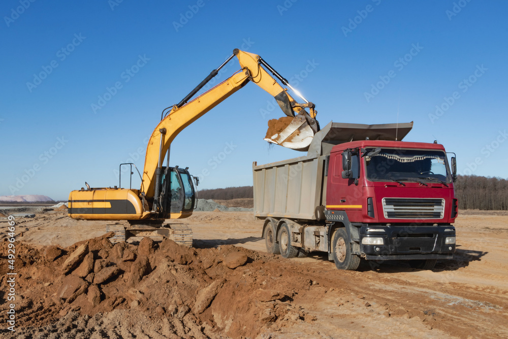 A powerful crawler excavator loads the earth into a dump truck against the blue sky. Development and removal of soil from the construction site. A powerful crawler excavator loads the earth into a dump truck against the blue sky. Development and removal of soil from the construction site.