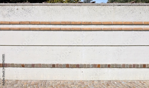 White concrete boundary wall decorated with horizontal strips of bricks and porphyry cubes. Background and texture.