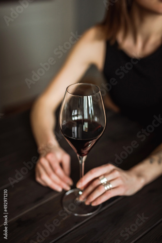 A close-up of a glass of red wine in the hands of a caucasian young woman, sitting at the wooden table