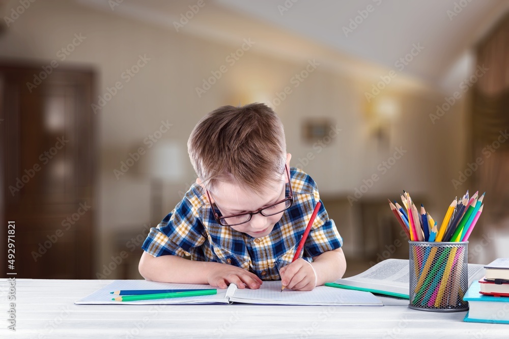 Smiling child school doing homework while sitting at desk at home, happy kid practicing handwriting in notebook, learning in home Smiling child school doing homework while sitting at desk at home, happy kid practicing handwriting in notebook, learning in home