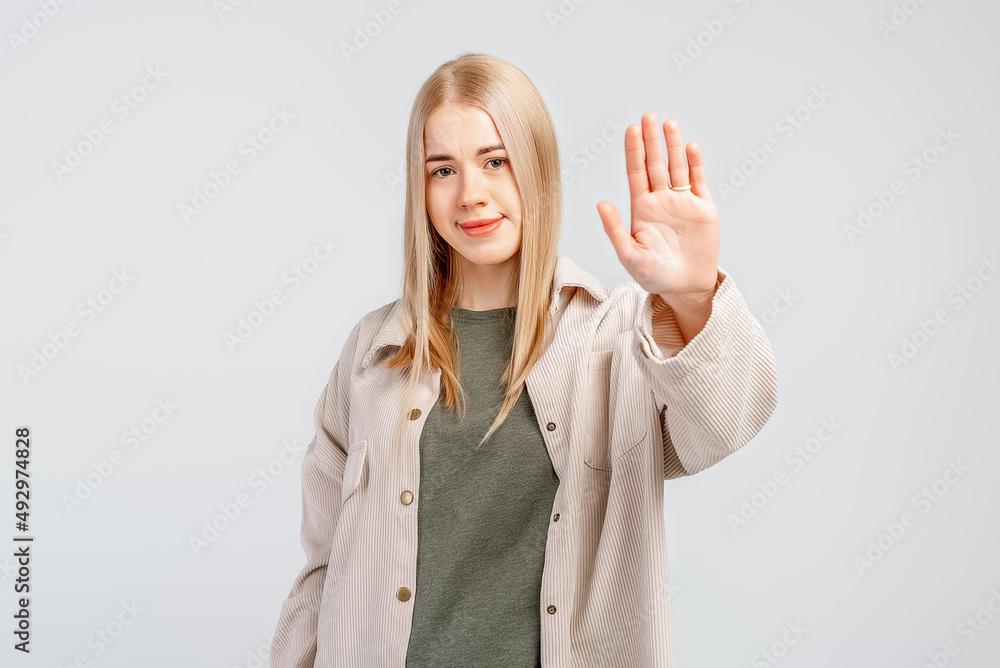 Portrait of a serious young blonde woman standing with outstretched hand showing stop gesture, permission denied, gray background Portrait of a serious young blonde woman standing with outstretched hand showing stop gesture, permission denied, gray background