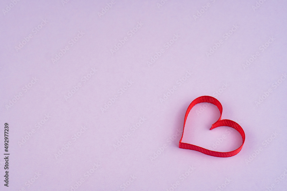 Top view Valentine's Day concept with copy space. Red ribbon heart on purple papper background Top view Valentine's Day concept with copy space. Red ribbon heart on purple papper background