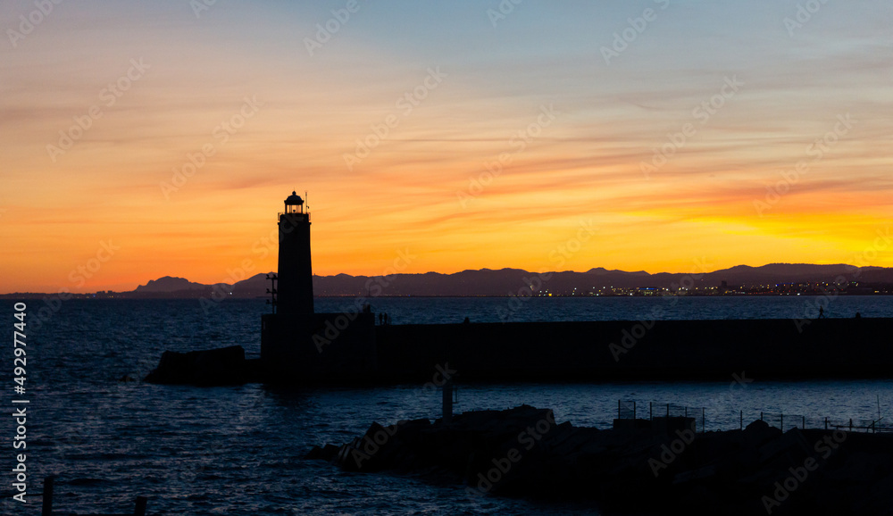 Sunset landscape that capture the sea, lighthouse and mountains silhouettes from the city of Nice, France.
