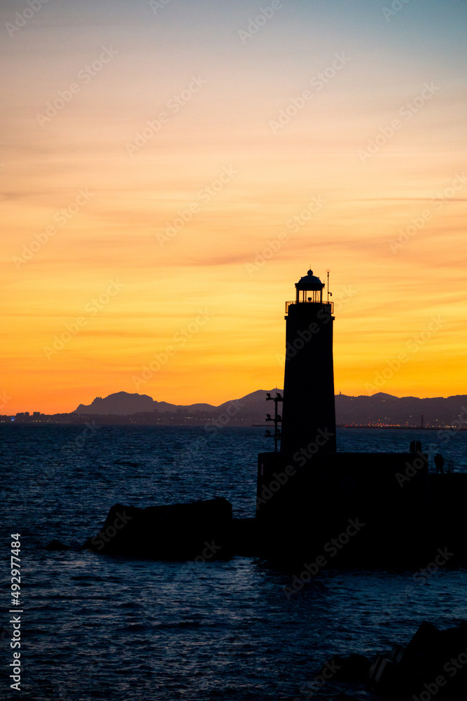 Beautiful nightly seascape with lighthouse, sea, mountains and colorful sky at the sunset.