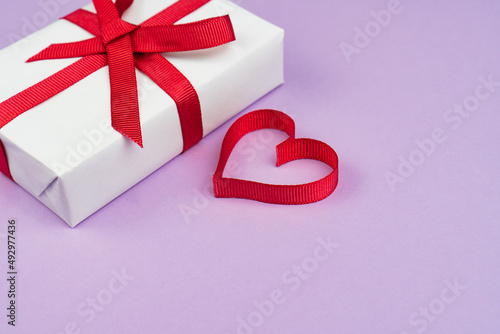 Valentine's Day or birthday concept with copy space. Red ribbon heart and gift box on purple papper photo