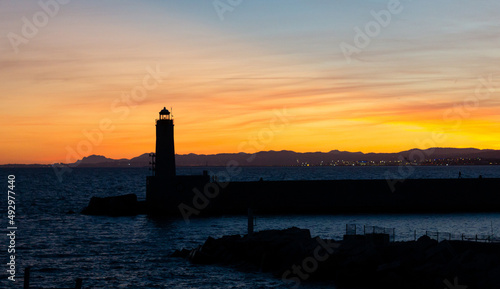 Sunset landscape that capture the sea, lighthouse and mountains silhouettes from the city of Nice, France.