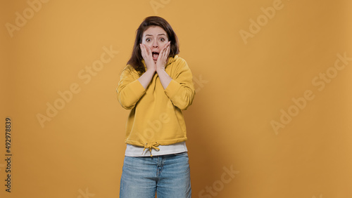 Fotografie Portrait of woman being scared doing hand gesture touching face in fear feeling frightened and afraid over yellow background