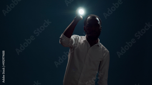 Young person sitting in the dark and using flashlight to search around, looking for evidence. Male detective taking risk and holding lantern to investigate and examine creepy sound. photo